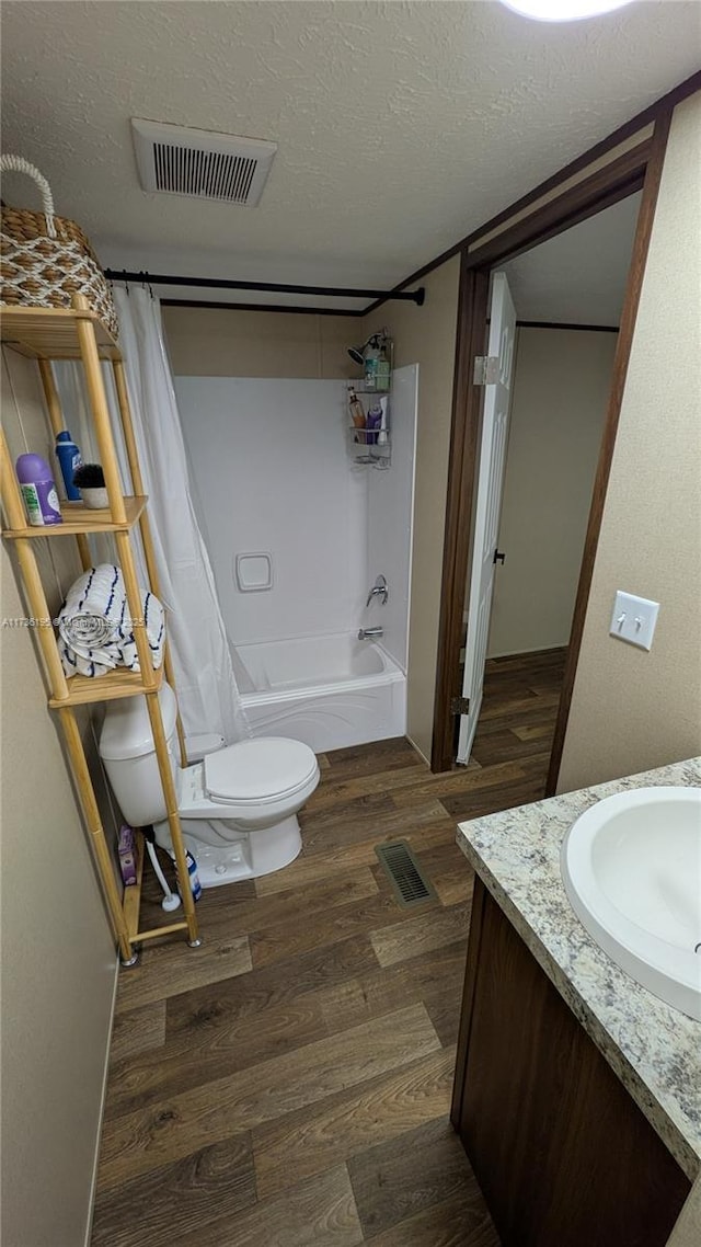 full bathroom featuring wood-type flooring, vanity, toilet, shower / bath combo, and a textured ceiling