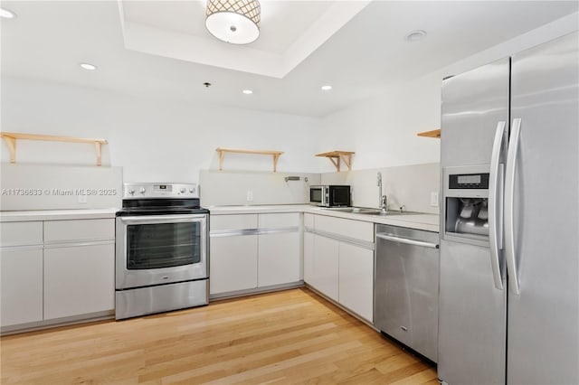 kitchen featuring sink, light wood-type flooring, appliances with stainless steel finishes, a raised ceiling, and white cabinets