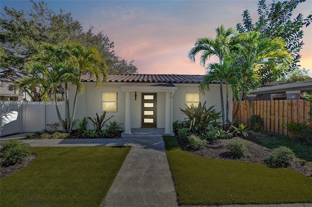 view of front of home with stucco siding, a tile roof, a lawn, and fence