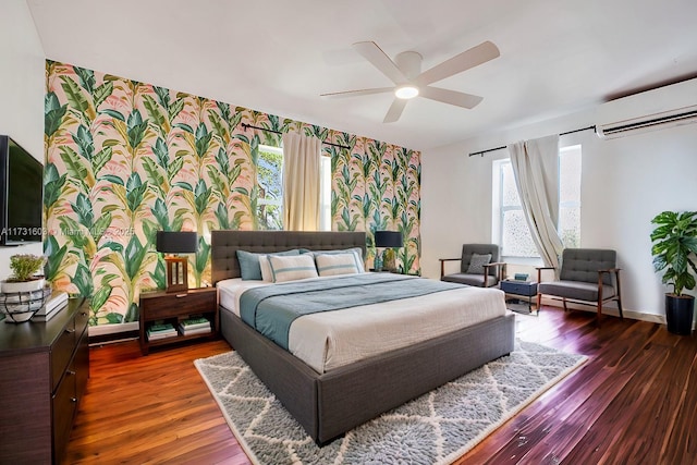 bedroom featuring an AC wall unit, multiple windows, wood finished floors, and wallpapered walls