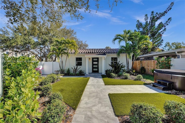 view of front of property featuring a tile roof, fence, a hot tub, and a front lawn