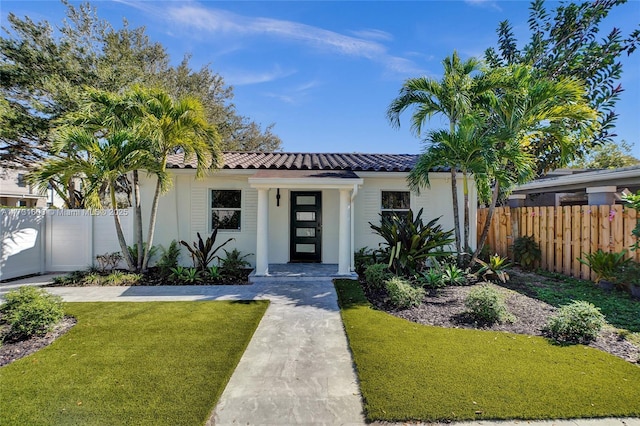 view of front of home with a front yard, a tile roof, fence, and stucco siding