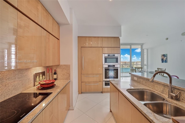 kitchen featuring tasteful backsplash, sink, light stone countertops, stainless steel double oven, and black electric cooktop