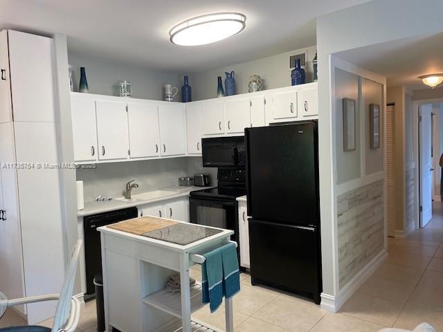 kitchen with sink, white cabinets, decorative backsplash, light tile patterned floors, and black appliances