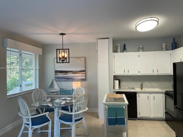 kitchen featuring sink, black appliances, hanging light fixtures, light tile patterned floors, and white cabinets