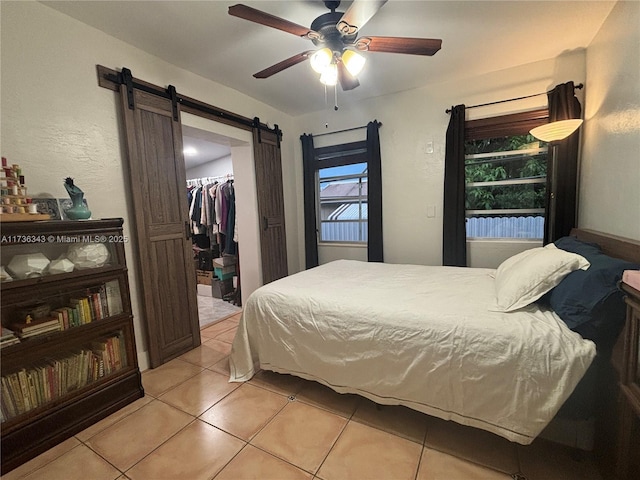 bedroom with light tile patterned flooring, a spacious closet, ceiling fan, a barn door, and a closet