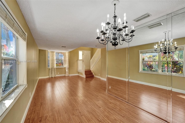 unfurnished living room featuring a notable chandelier, wood-type flooring, and a textured ceiling