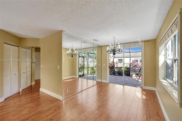 unfurnished dining area with a textured ceiling, a notable chandelier, and light hardwood / wood-style floors