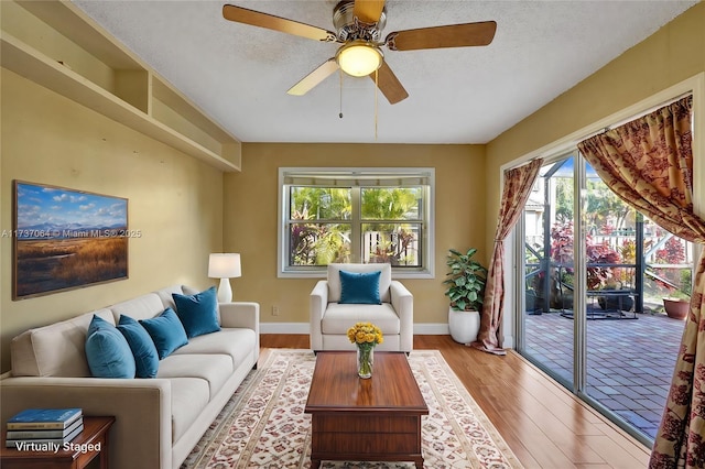 living room with ceiling fan, a textured ceiling, and light wood-type flooring