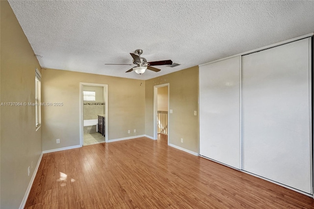 unfurnished bedroom with ensuite bath, a textured ceiling, light wood-type flooring, a closet, and ceiling fan