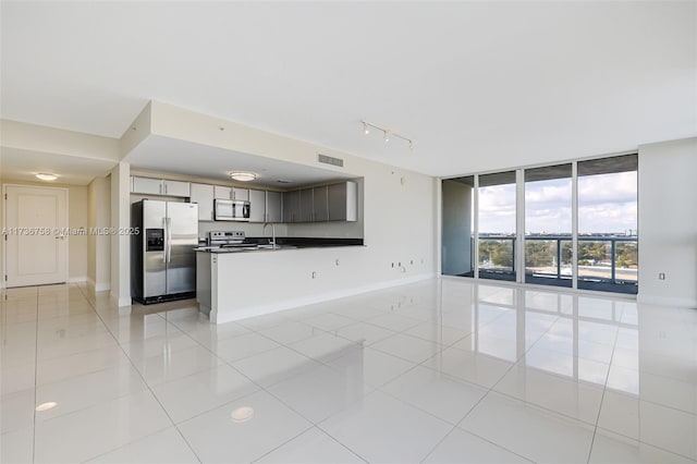 kitchen with sink, appliances with stainless steel finishes, floor to ceiling windows, light tile patterned flooring, and kitchen peninsula