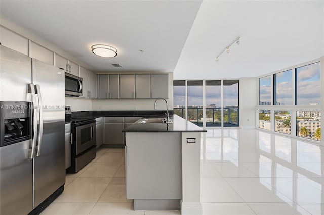 kitchen with an island with sink, sink, expansive windows, light tile patterned floors, and stainless steel appliances