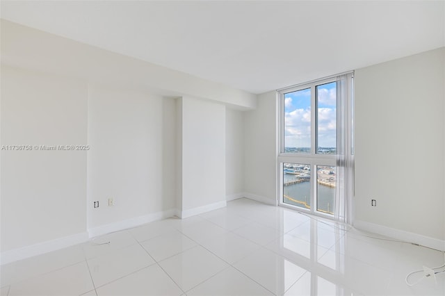 unfurnished room with floor to ceiling windows, a water view, and light tile patterned floors