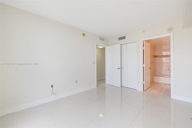 unfurnished bedroom with ensuite bathroom, light tile patterned floors, and a closet