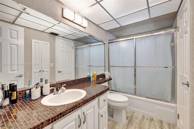 full bathroom with hardwood / wood-style flooring, a paneled ceiling, combined bath / shower with glass door, vanity, and toilet