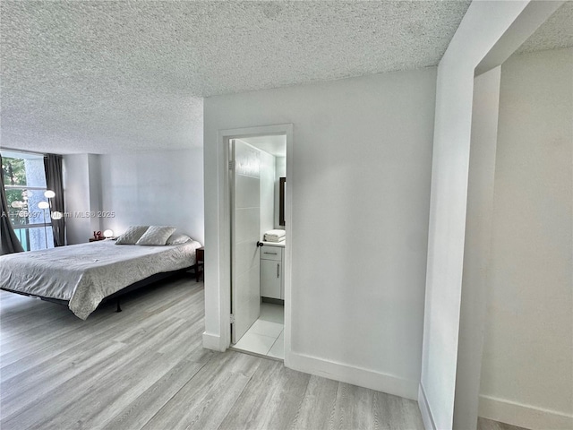 1000 Parkview Dr Unit 202, Hallandale Beach, FL 33009 - bedroom featuring a textured ceiling, ensuite bath, light wood-style flooring, and baseboards