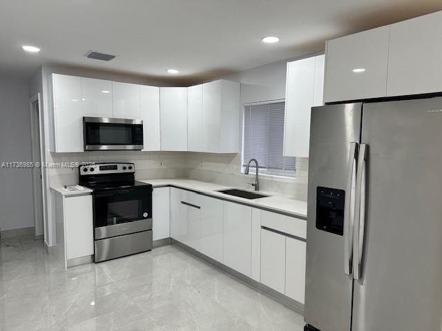 kitchen featuring stainless steel appliances, sink, decorative backsplash, and white cabinets