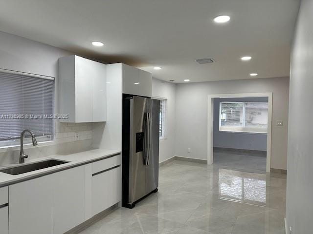 kitchen with tasteful backsplash, sink, stainless steel fridge, and white cabinets