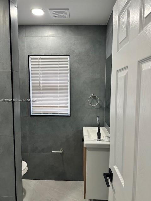 bathroom featuring vanity, tile walls, and toilet