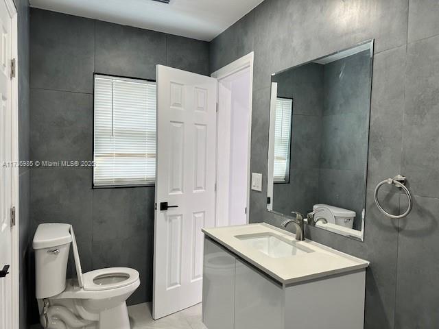 bathroom featuring vanity, tile walls, and toilet