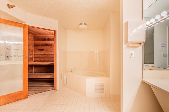 bathroom with a relaxing tiled tub, tile patterned flooring, and a textured ceiling