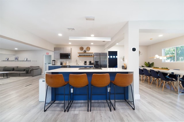 kitchen featuring stainless steel refrigerator with ice dispenser, a kitchen breakfast bar, sink, and light hardwood / wood-style flooring