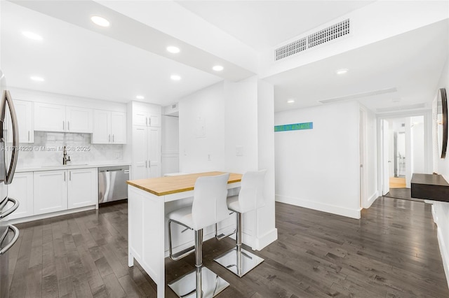 kitchen with dark wood-type flooring, a breakfast bar, wooden counters, dishwasher, and white cabinets