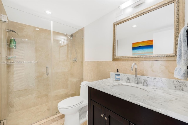 bathroom featuring a shower with door, vanity, tile walls, and toilet