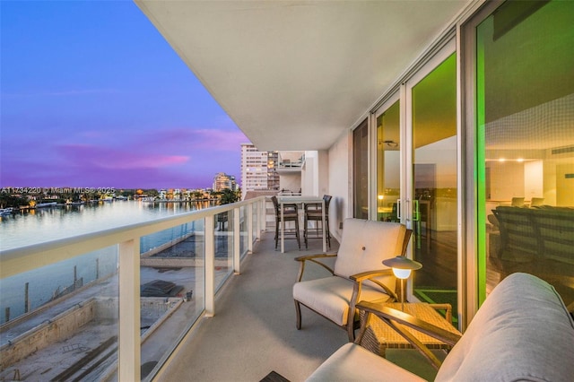 balcony at dusk featuring a water view