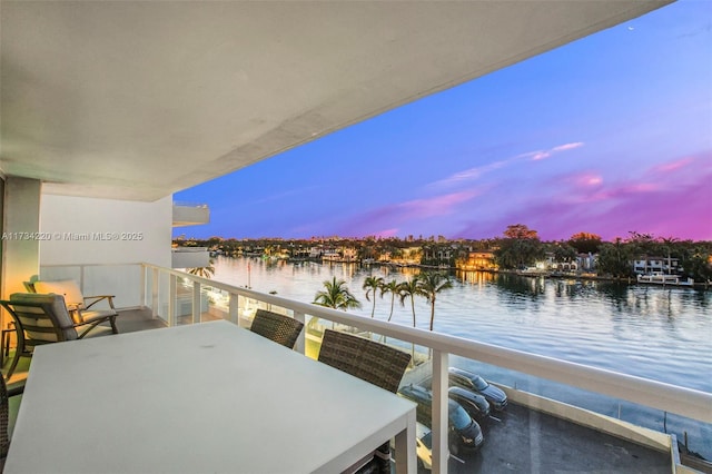 balcony at dusk featuring a water view