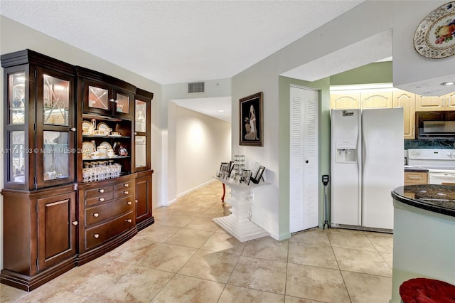 kitchen featuring dark brown cabinets, light tile patterned floors, a textured ceiling, and white appliances