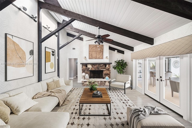 living room with high vaulted ceiling, beam ceiling, light wood-style flooring, a stone fireplace, and french doors