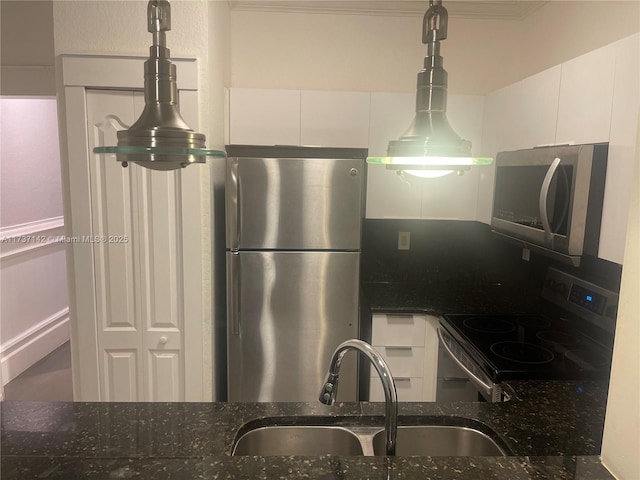 kitchen featuring sink, white cabinetry, hanging light fixtures, appliances with stainless steel finishes, and dark stone counters