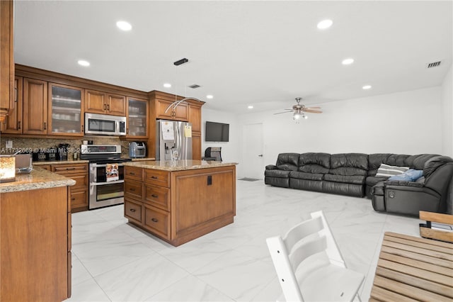 kitchen with a kitchen island, backsplash, hanging light fixtures, stainless steel appliances, and light stone countertops