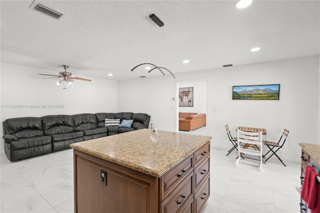 kitchen with ceiling fan, a center island, hanging light fixtures, and a textured ceiling