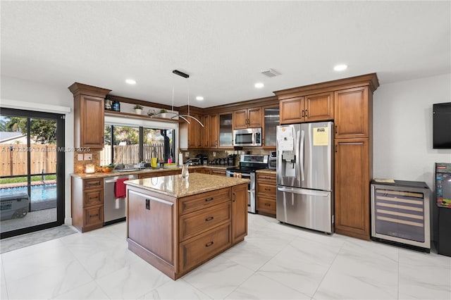 kitchen featuring beverage cooler, hanging light fixtures, a center island, stainless steel appliances, and light stone countertops