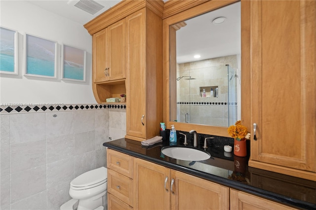 bathroom with vanity, a shower with shower door, tile walls, and toilet