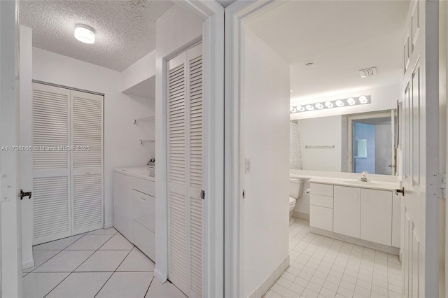 bathroom with toilet, a textured ceiling, vanity, independent washer and dryer, and tile patterned flooring