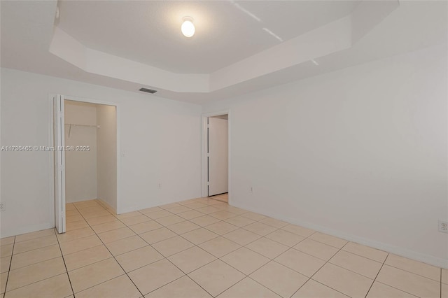 unfurnished bedroom with a closet, a spacious closet, light tile patterned floors, and a tray ceiling