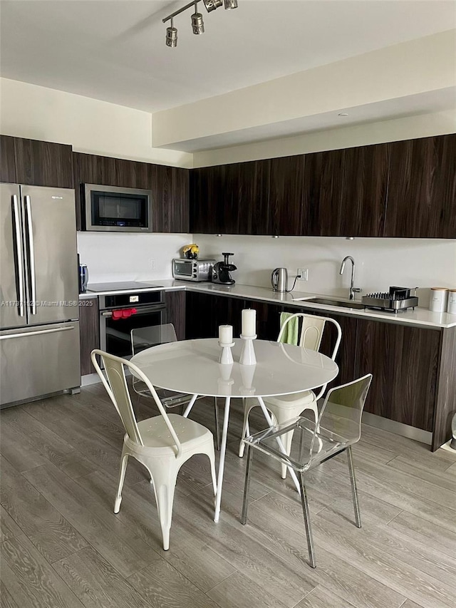 kitchen with stainless steel appliances, dark brown cabinets, sink, and light hardwood / wood-style flooring