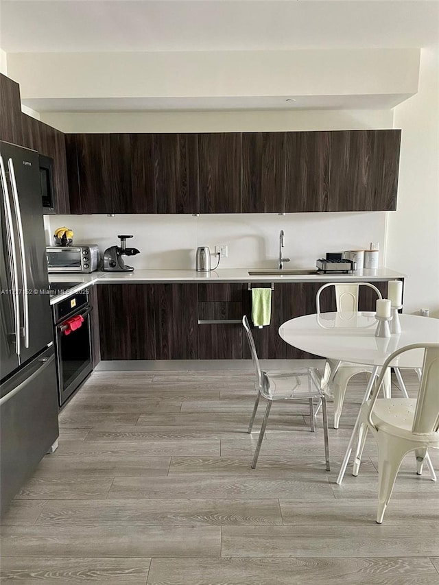 kitchen with dark brown cabinetry, sink, stainless steel appliances, and light wood-type flooring