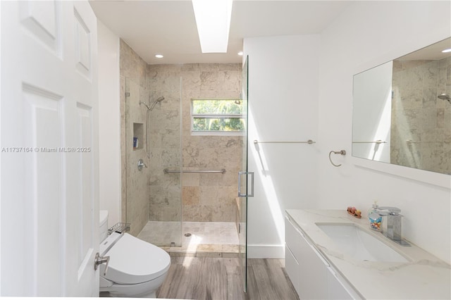 bathroom featuring toilet, wood-type flooring, a skylight, vanity, and a shower with door