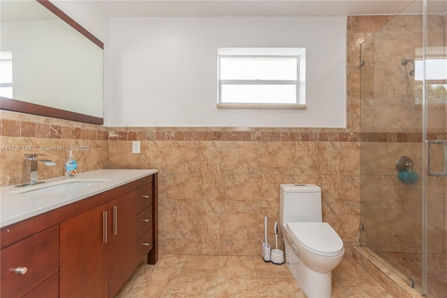 bathroom with vanity, toilet, a shower with shower door, and tile walls