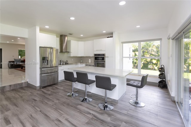 kitchen featuring white cabinets, stainless steel appliances, a breakfast bar, and wall chimney range hood