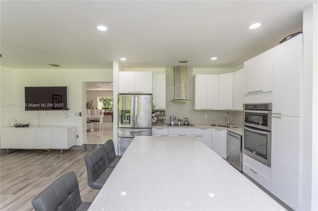 kitchen featuring white cabinets, stainless steel appliances, sink, and wall chimney exhaust hood