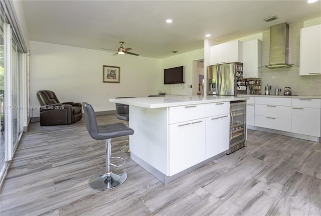 kitchen with white cabinetry, stainless steel fridge, wall chimney exhaust hood, and a kitchen island