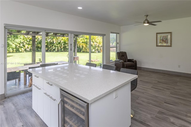 kitchen with wood-type flooring, a kitchen breakfast bar, a kitchen island, beverage cooler, and white cabinets