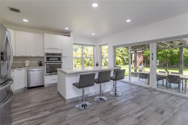 kitchen with white cabinetry, stainless steel appliances, a center island, and a kitchen bar