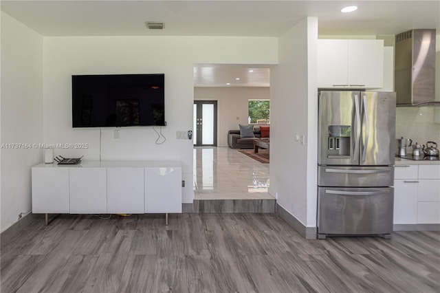 kitchen with white cabinetry, stainless steel fridge, backsplash, wall chimney range hood, and light wood-type flooring