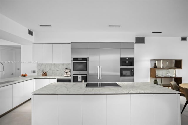 kitchen with white cabinetry, a center island, light stone counters, stainless steel double oven, and black electric cooktop